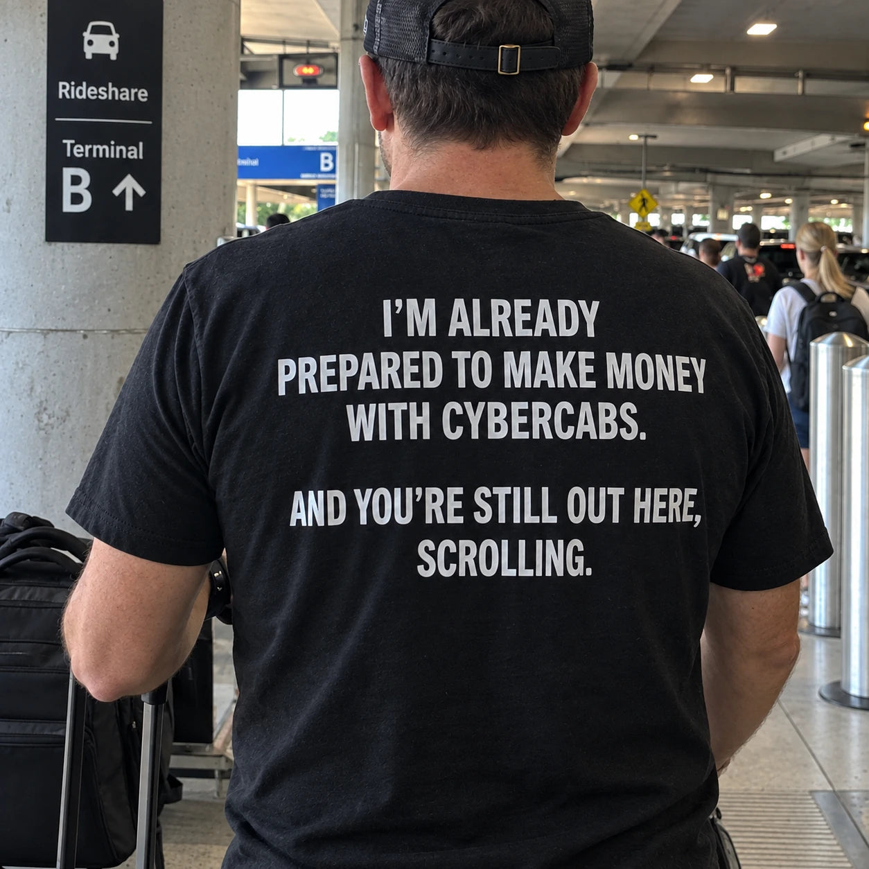 A man at an airport rideshare area wearing a shirt that reads I’M ALREADY PREPARED TO MAKE MONEY WITH CYBERCABS. AND YOU’RE STILL OUT HERE, SCROLLING.